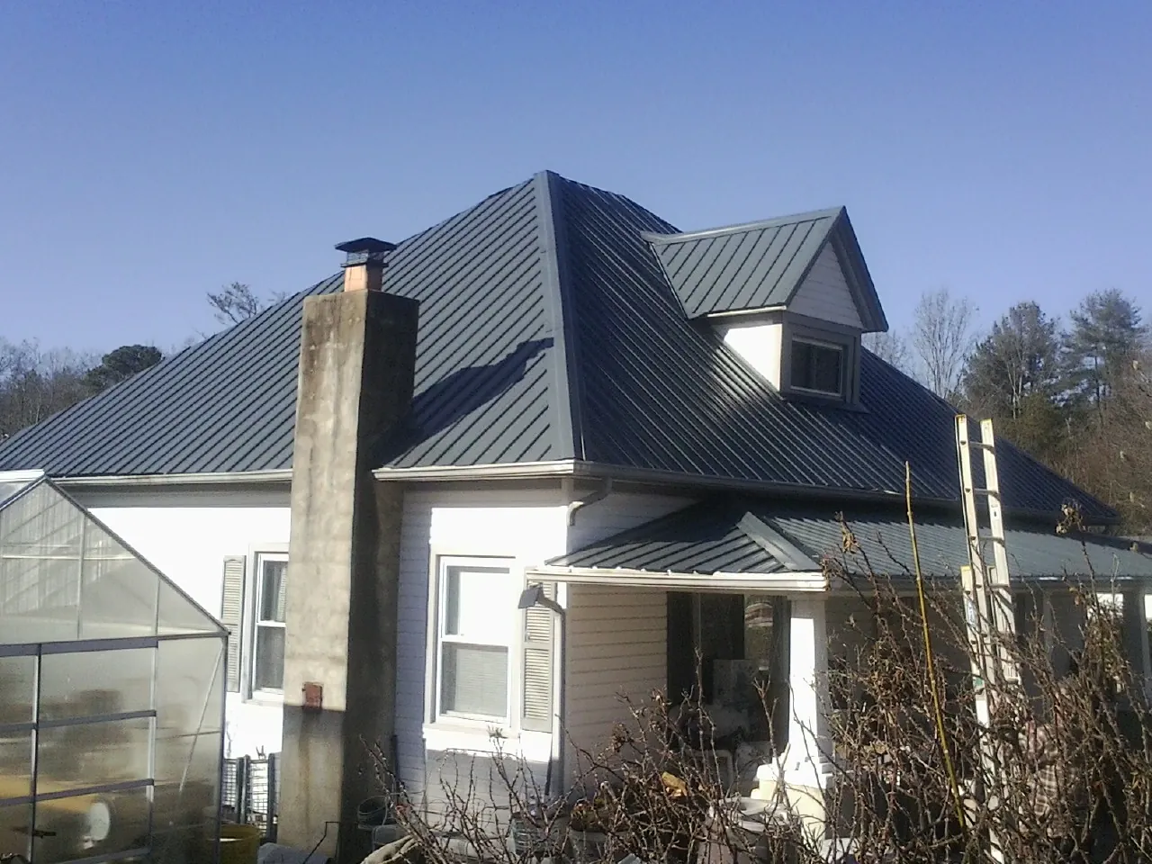 Dark blue standing seam metal roof on a white farmhouse with dormer — Slate & Tile Roof Repair by Roofing Brothers in Anderson