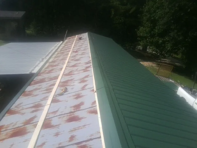 Old rusted panels beside newly installed green metal roofing — Wind Damage Roof Repair by Roofing Brothers in Anderson