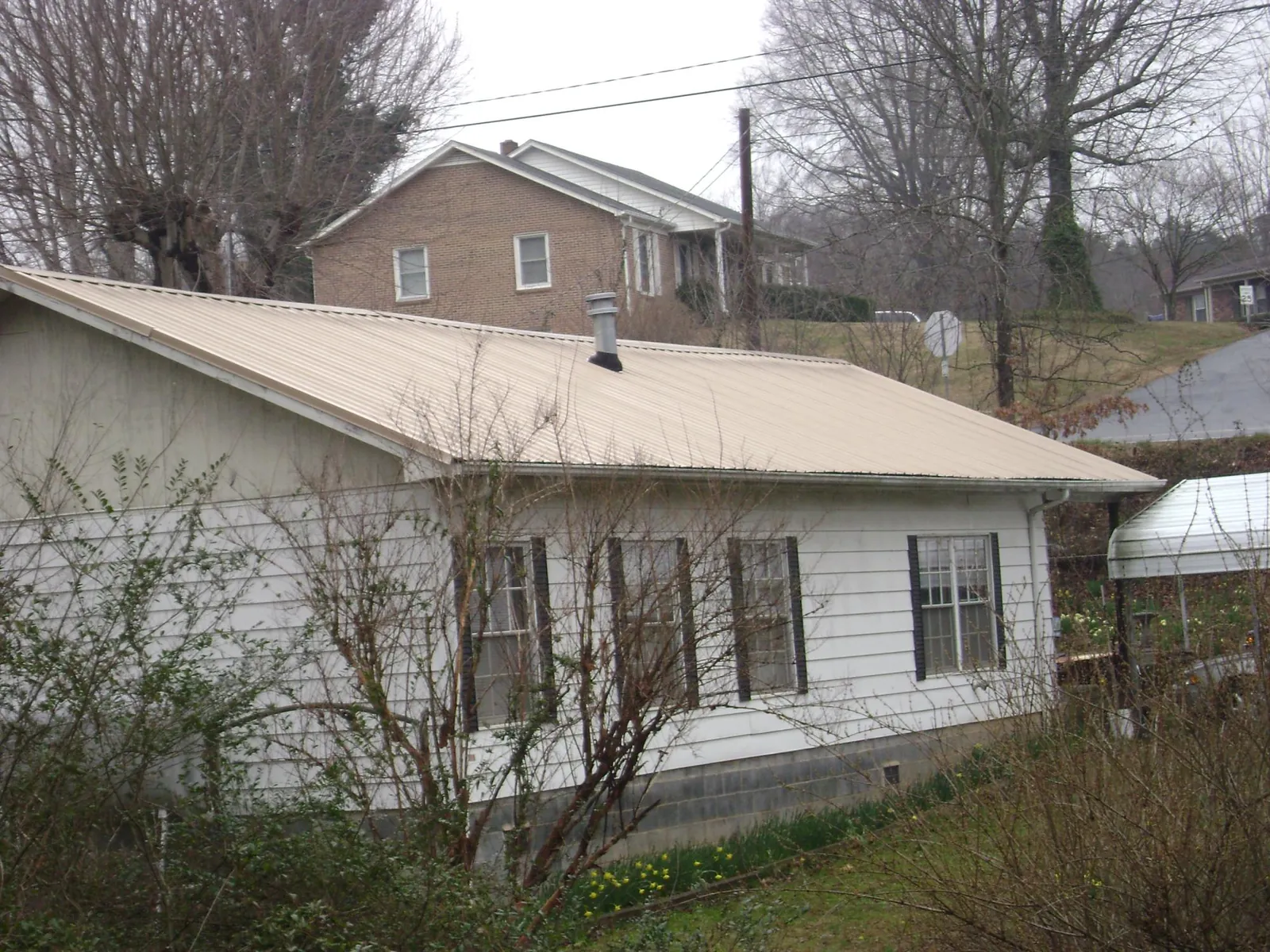 Tan metal roof on a white sided house set into a hillside — Commercial Roofing by Roofing Brothers in Anderson